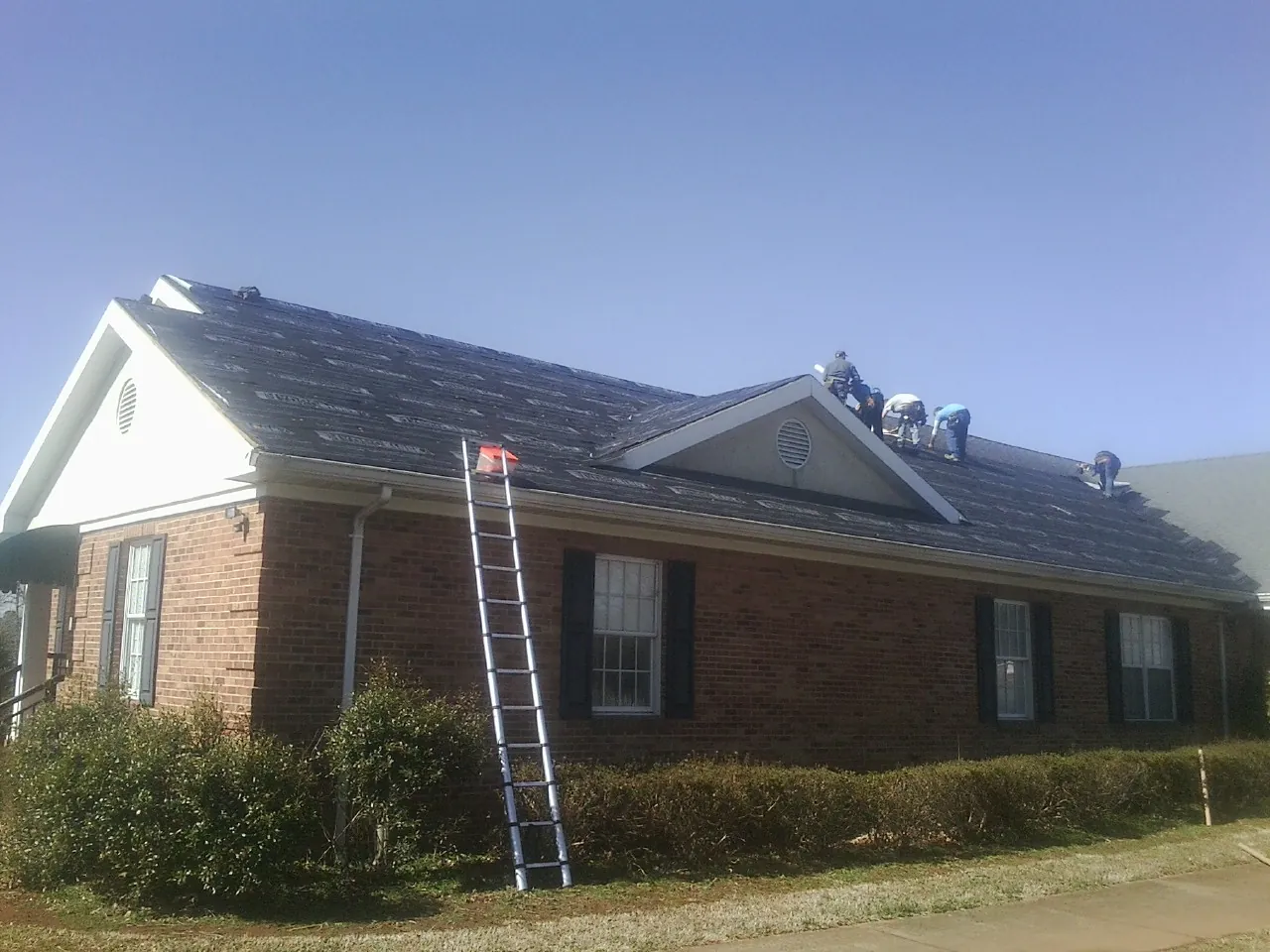 Crew tearing shingles off a brick ranch roof with a ladder set — Emergency Roof Repair work by our crew in Cochranton