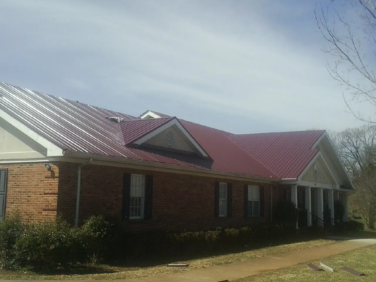 Red metal roof with gabled entries on a long brick building, from a Hail Damage Roof Repair job in Cochranton