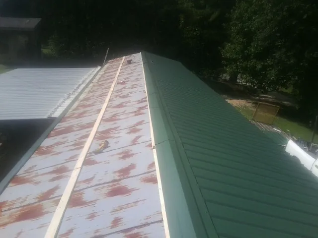 Old rusted panels beside newly installed green metal roofing — Wind Damage Roof Repair by Roofing Brothers in Cochranton