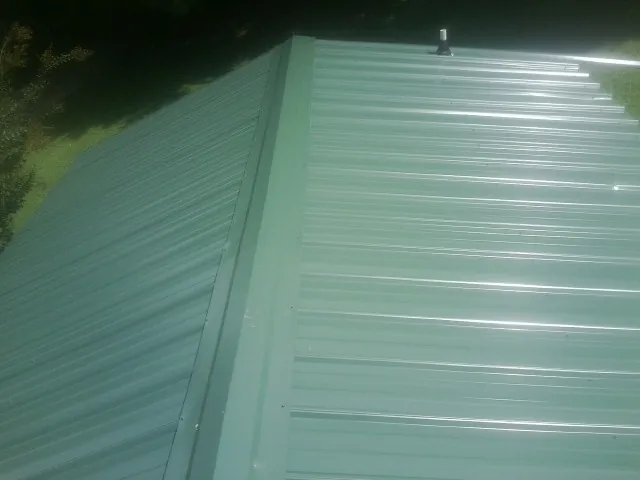 New green metal panels meeting at the ridge of a roof — Flat Roof Repair work by our crew in Cochranton