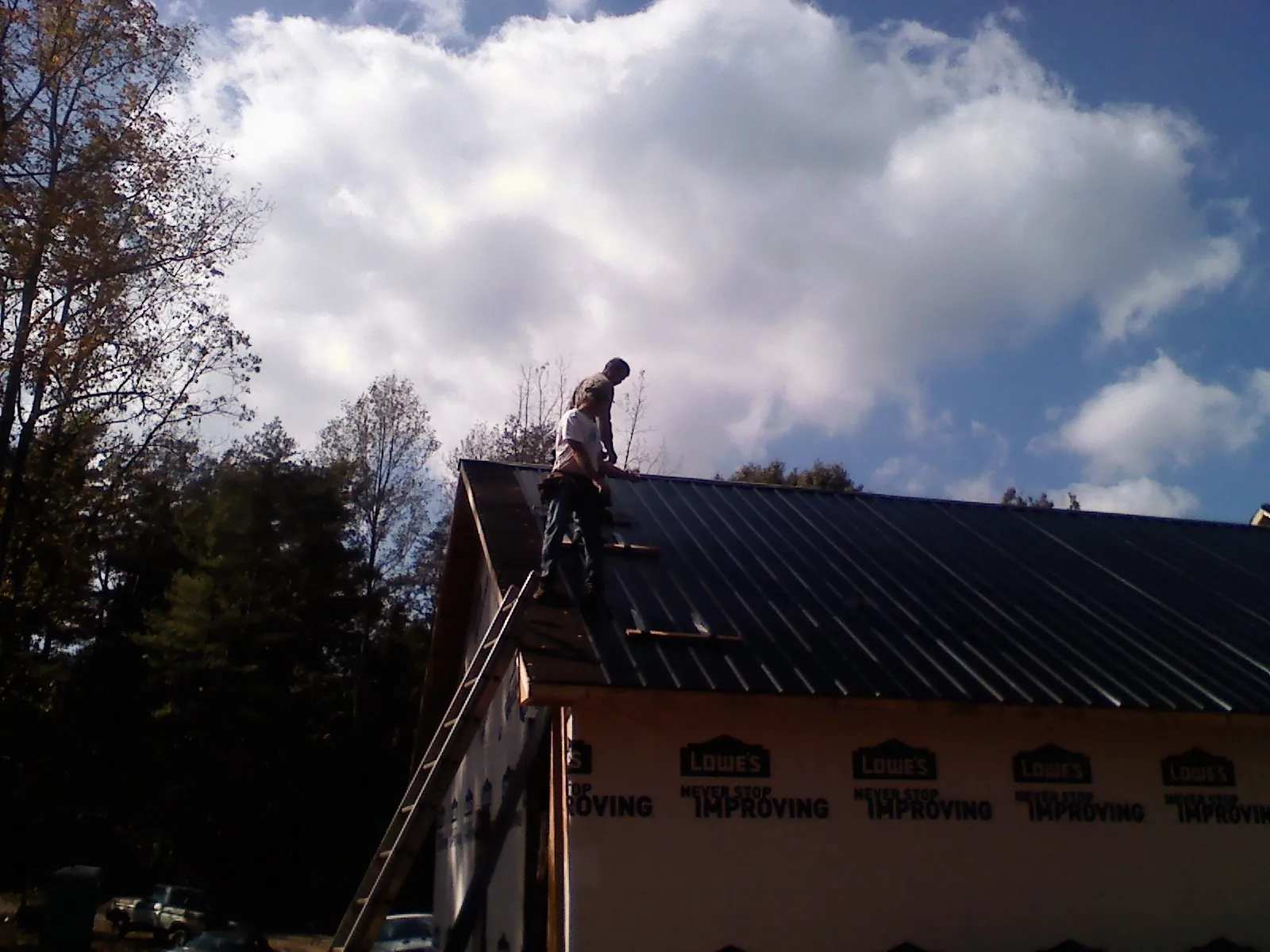 Roofer fastening dark metal panels high against a cloudy sky, from a Roof Inspection job in Cochranton