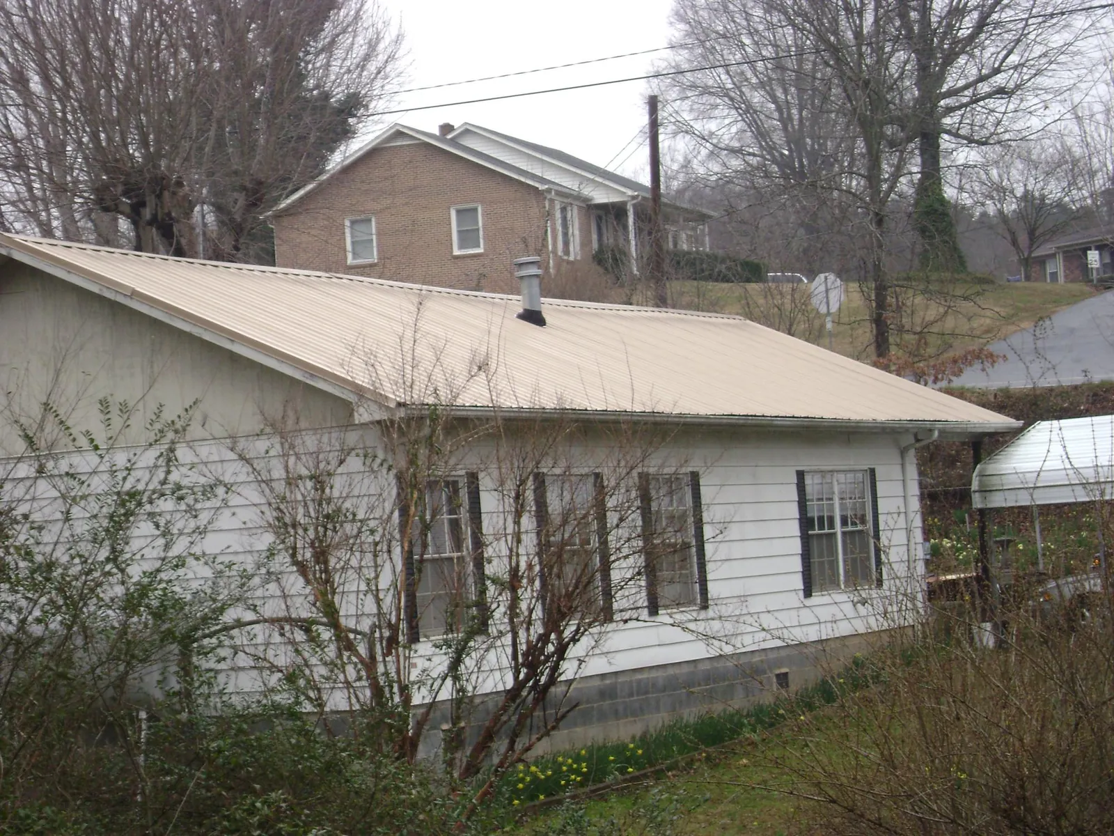 Tan metal roof on a white sided house set into a hillside — Commercial Roofing by Roofing Brothers in Cochranton