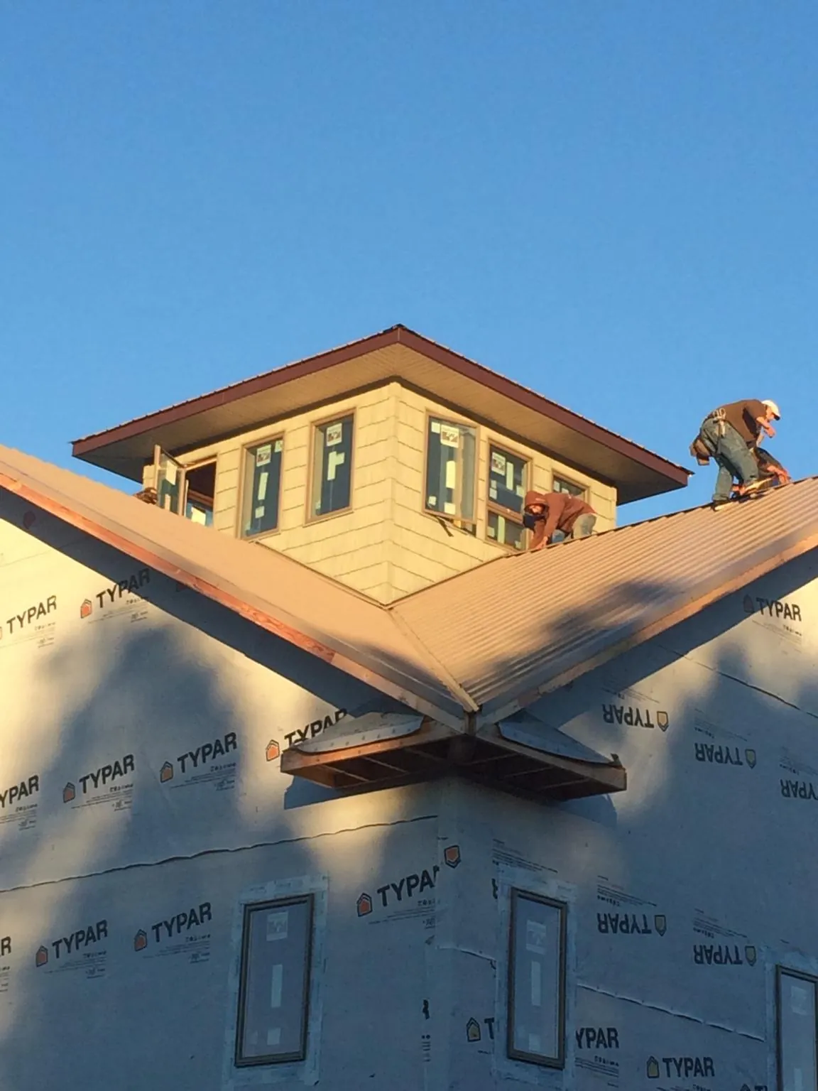 Roofers working around a rooftop cupola on a new metal roof at sunset — Roof Waterproofing in Cochranton by Roofing Brothers